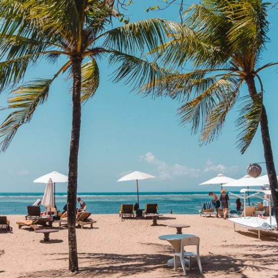 Sanur Beach, with palm trees, while umbrellas and sun loungers (top Bali travel tips).