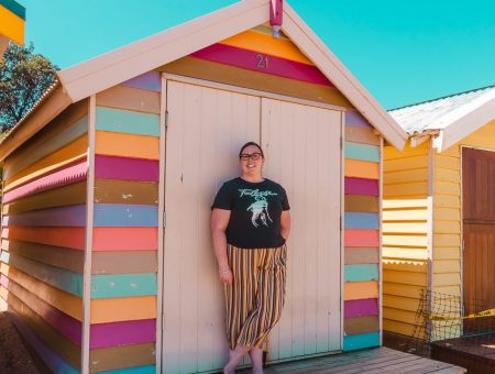 Standing in front of a pastel striped beach hut at the Brighton Bathing Boxes in Melbourne, Australia - one of the best free things to do in Melbourne!